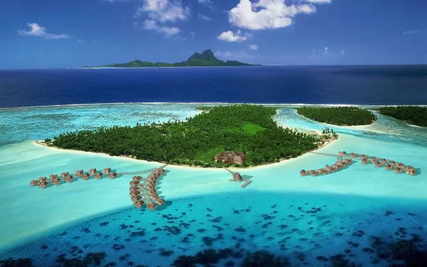 HD desktop wallpaper of a tropical island with lush trees, overwater huts, and clear ocean waters under a blue sky, showcasing serene island photography.
