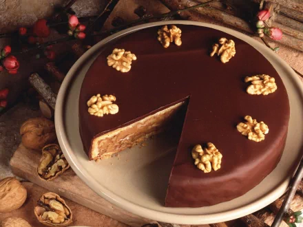 HD desktop wallpaper showing a rich chocolate cake topped with walnut halves, with a slice removed to reveal its layered interior.