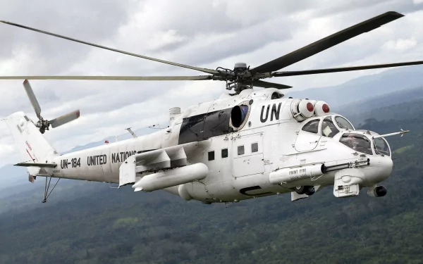 HD desktop wallpaper of a white Mil Mi-24 military helicopter marked with UN insignia flying over a forested landscape under a cloudy sky.
