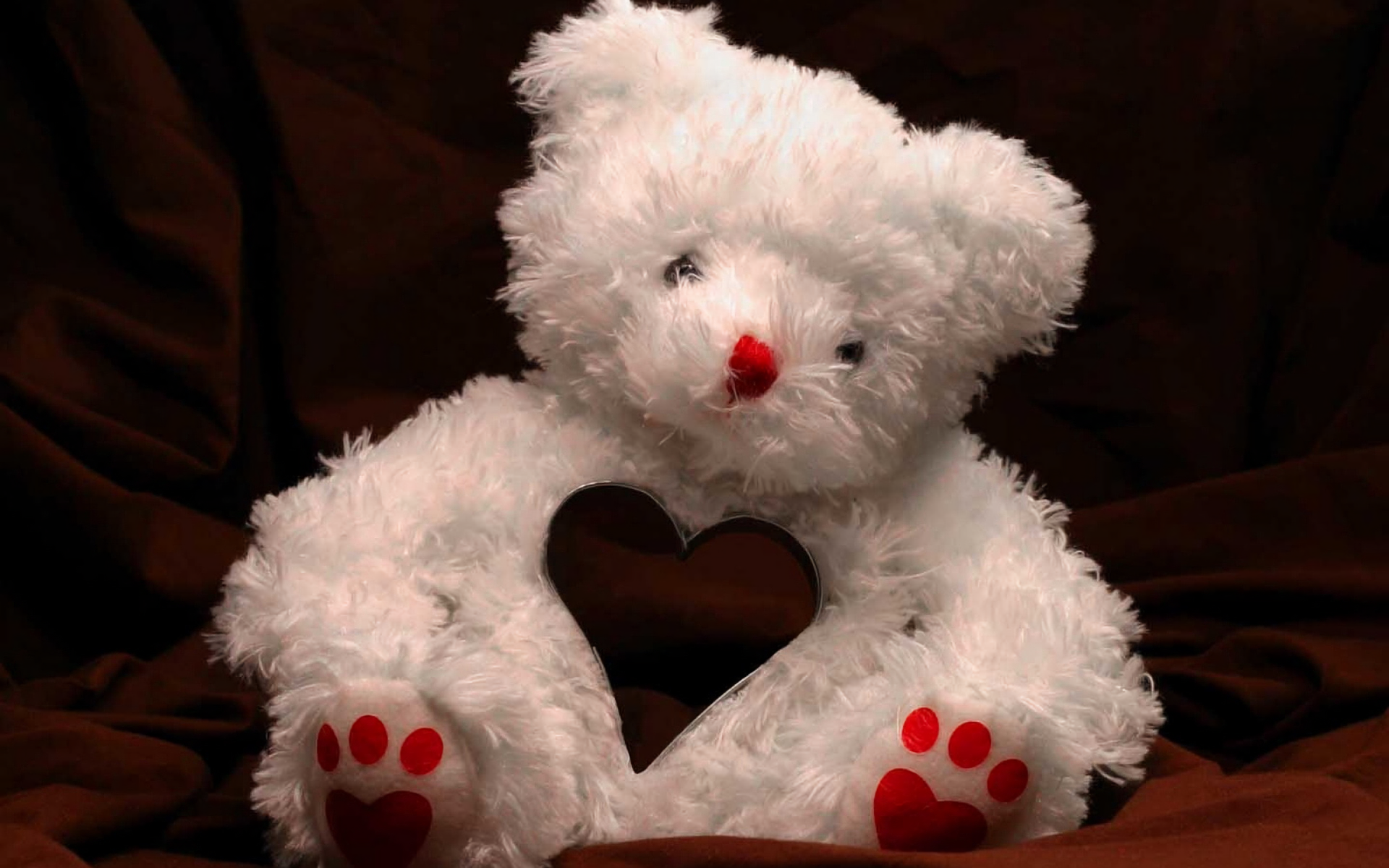 White teddy bear with red nose and paw prints holding a heart-shaped cutout, set against a dark background, themed for Valentine's Day holiday as an HD PC desktop wallpaper.