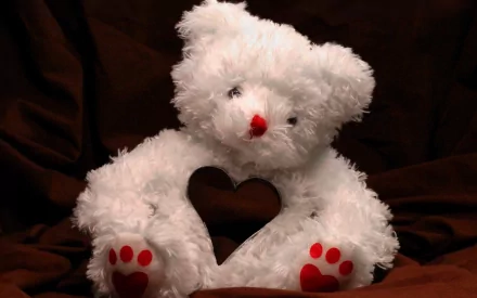 White teddy bear with red nose and paw prints holding a heart-shaped cutout, set against a dark background, themed for Valentine's Day holiday as an HD PC desktop wallpaper.