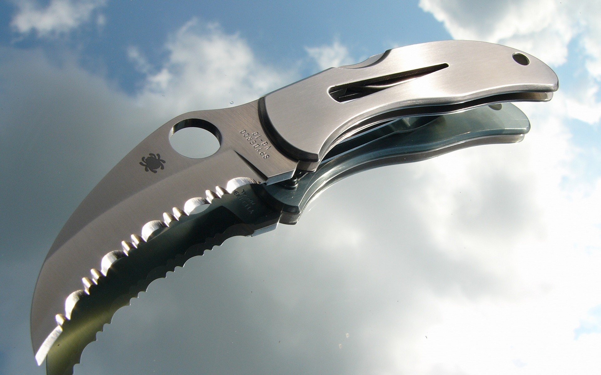 HD PC desktop wallpaper featuring a close-up of a man-made folding knife with a serrated edge against a cloudy sky background.