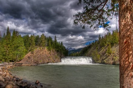 A stunning waterfall cascades through rugged terrain in the Canadian Rockies, surrounded by lush greenery and dramatic clouds, showcasing the natural beauty of the landscape.