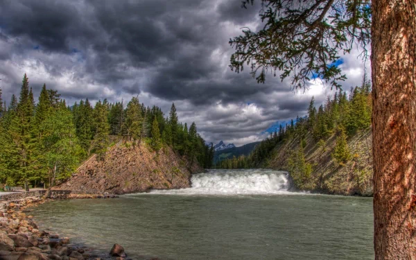 A stunning waterfall cascades through rugged terrain in the Canadian Rockies, surrounded by lush greenery and dramatic clouds, showcasing the natural beauty of the landscape.