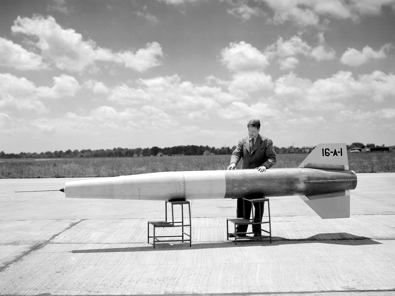 A black-and-white image of a man in a suit standing next to a missile on a runway, featuring military themes. This HD image serves as a striking desktop wallpaper and background.