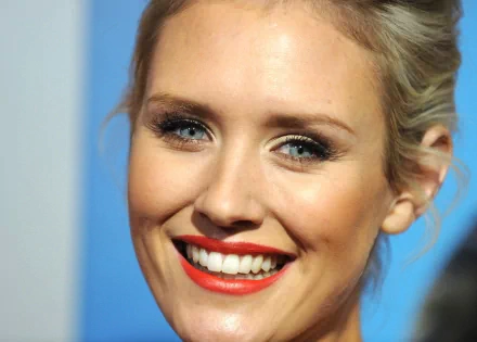Close-up HD desktop wallpaper of woman Nicky Whelan smiling with bright red lipstick and natural makeup against a soft blue background.