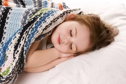 An HD desktop wallpaper featuring a child peacefully sleeping under a colorful, striped blanket, with a serene expression on their face.