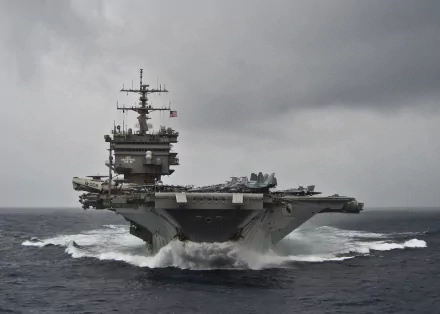 HD desktop wallpaper showing the USS Enterprise (CVN-65) aircraft carrier cutting through waves under a cloudy sky, highlighting its military power and presence at sea.
