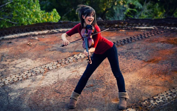 Lindsey Stirling plays the violin joyfully on a textured, rust-colored surface, surrounded by lush greenery, captured in an HD desktop wallpaper.