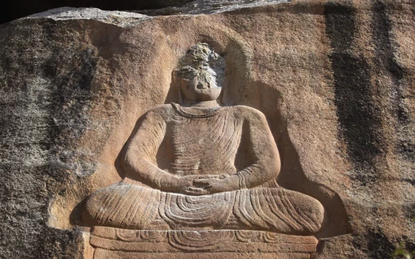 4K Ultra HD PC desktop background of a man-made stone Buddha statue carved into a weathered rock face, seated in meditation with carved robes and strong light-and-shadow texture.