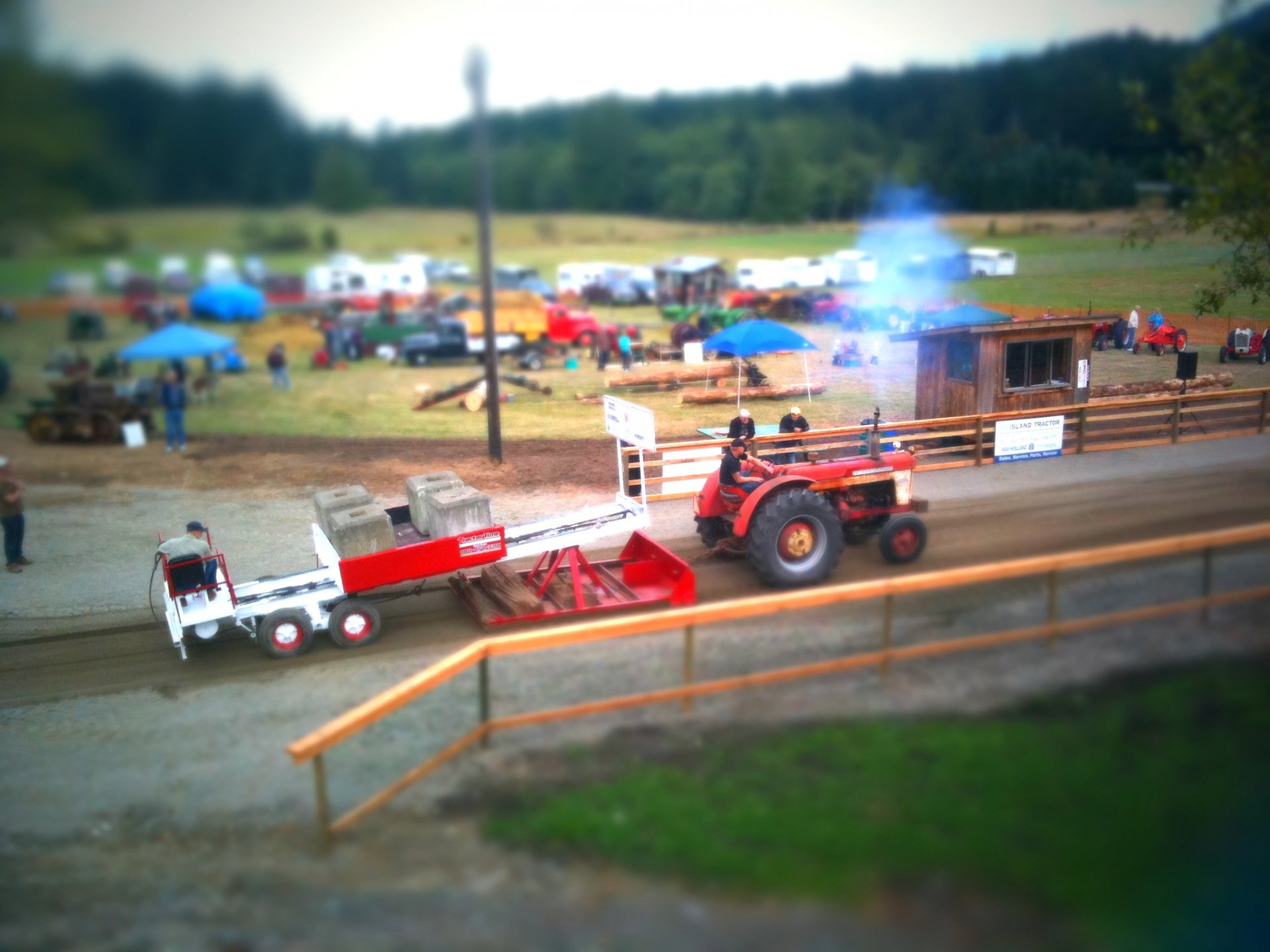 HD desktop wallpaper showing a tractor pulling a sled on a dirt track with spectators and tents in the background at an outdoor event.