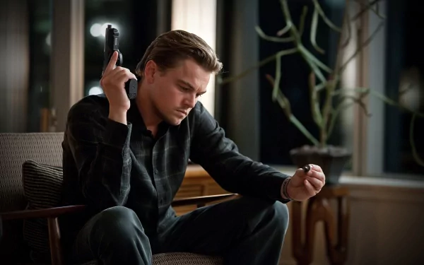 Leonardo DiCaprio in a suspenseful moment from the movie *Inception*, seated with a contemplative expression, holding a gun and a small object, set against a stylish backdrop.