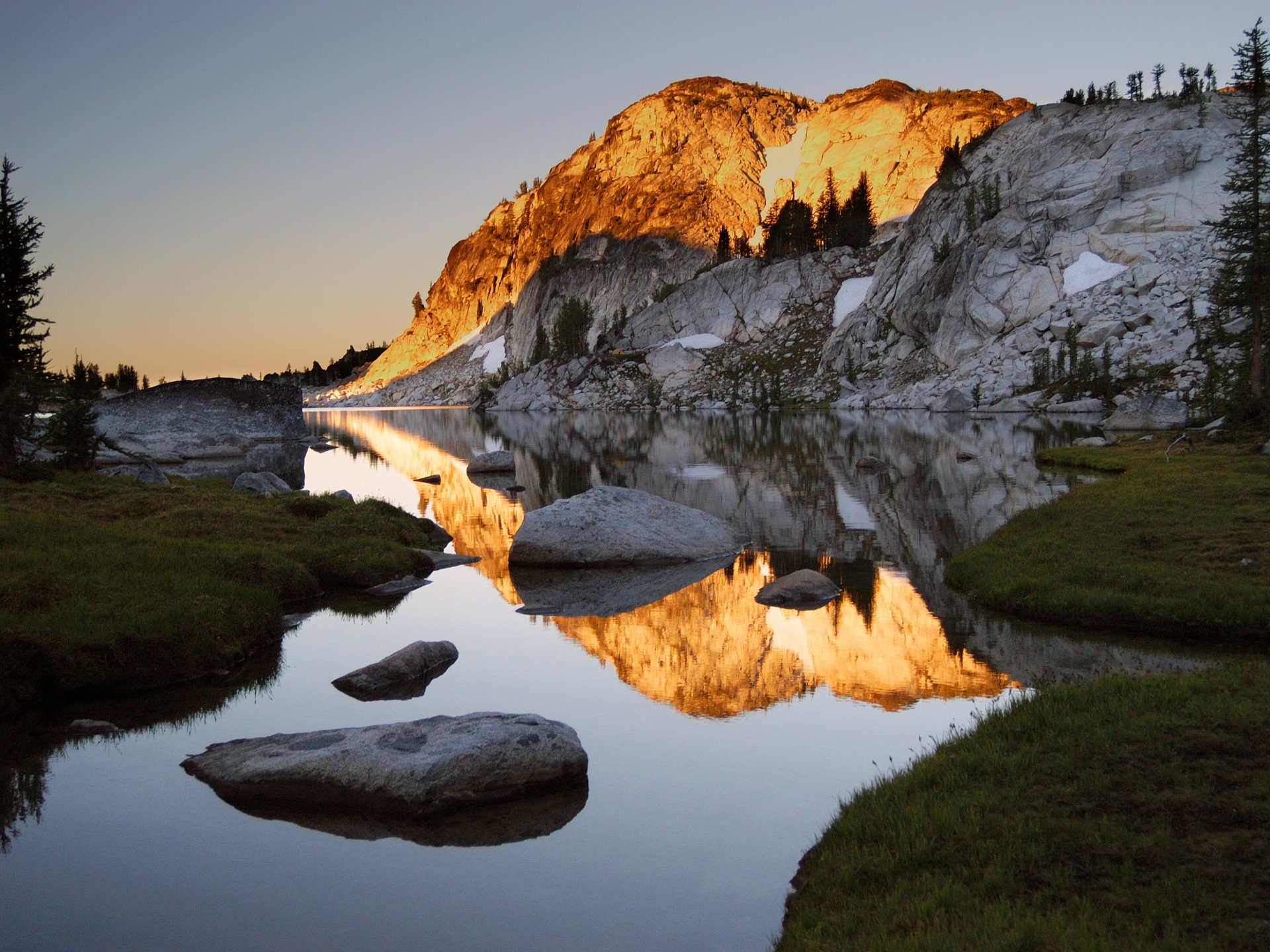 A stunning HD wallpaper showcasing a serene mountain landscape at sunrise, with vibrant rock reflections in a peaceful lake surrounded by lush greenery.