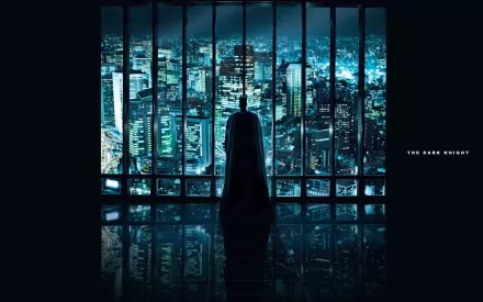 HD desktop wallpaper featuring Batman standing in front of a large window overlooking a cityscape at night, with The Dark Knight text on the right side.