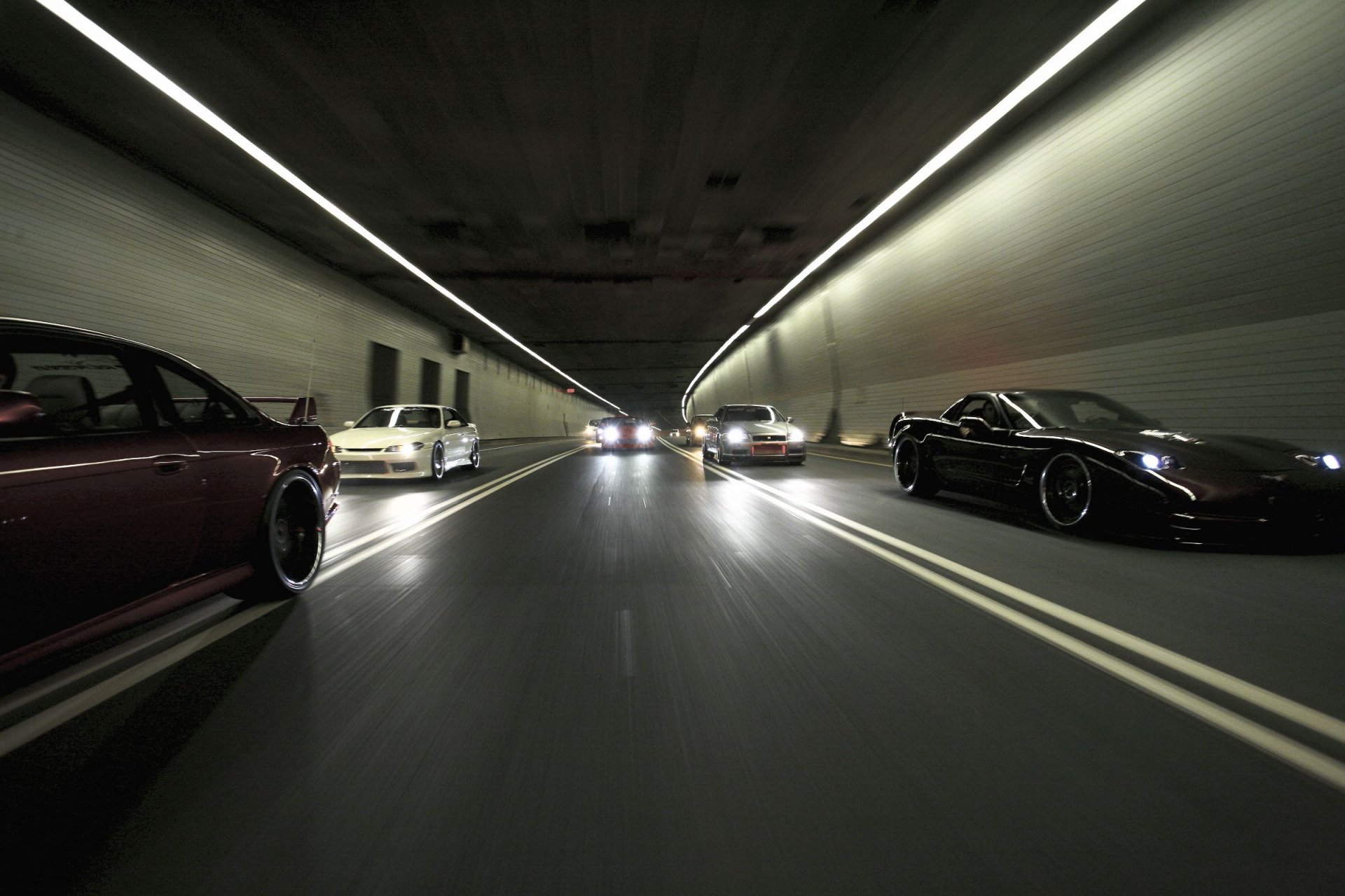 A dynamic scene of multiple cars speeding through a well-lit tunnel, showcasing the thrill of automotive energy. This HD image serves as a striking desktop wallpaper and background.
