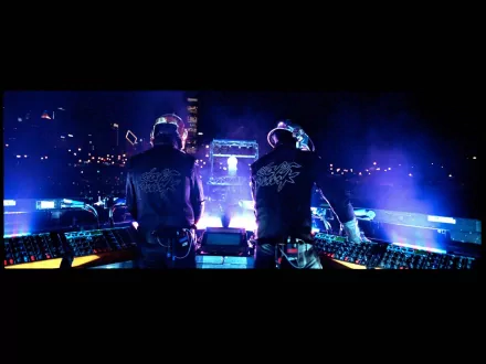 Daft Punk performing with illuminated DJ equipment in a vibrant, neon-lit atmosphere. This HD desktop wallpaper showcases their iconic robotic helmets and stage presence.