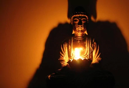 HD desktop wallpaper of a serene Buddha statue holding a glowing light in a dark background, reflecting Buddhist religious themes.
