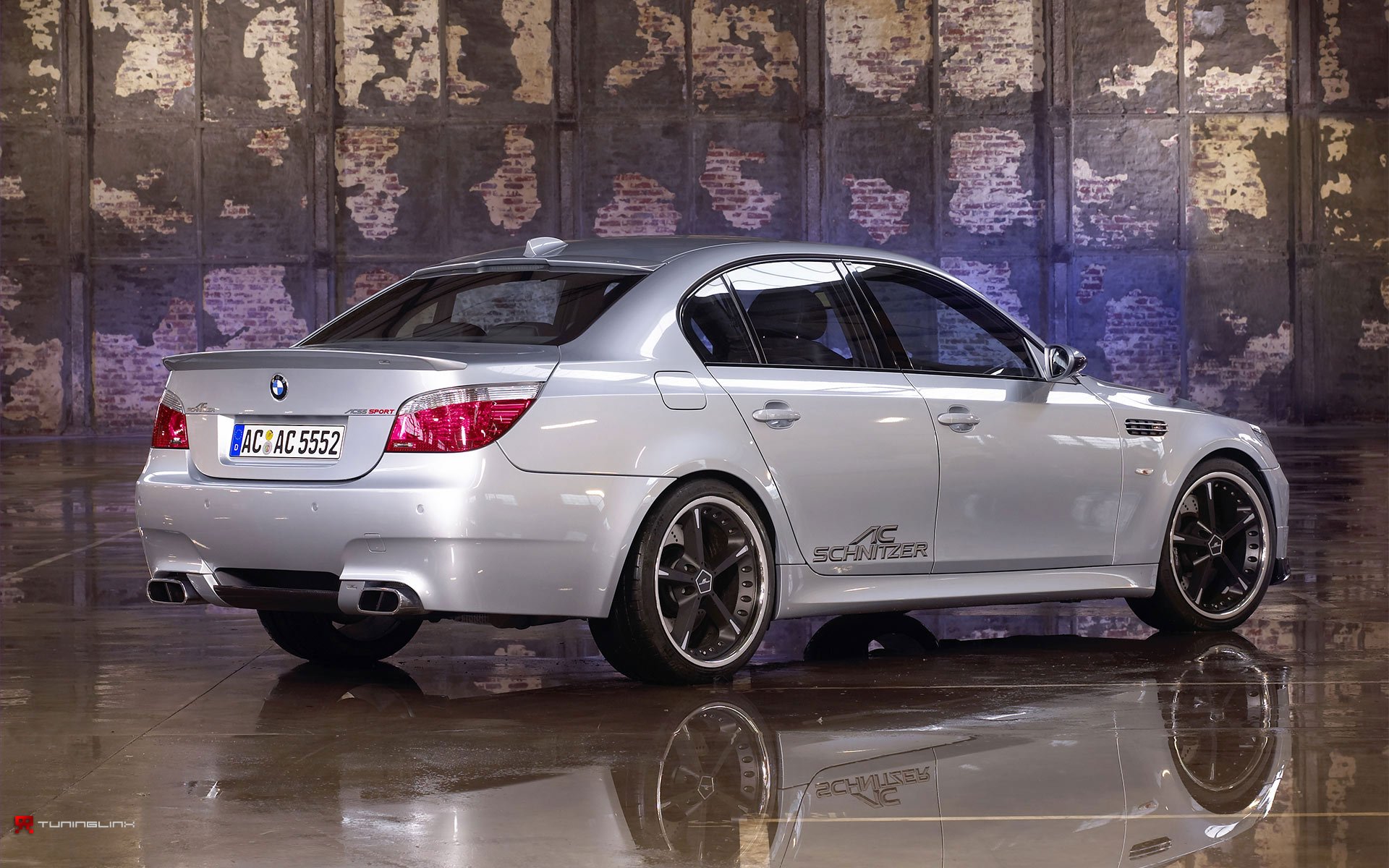 HD desktop wallpaper featuring a silver BMW 5 Series sedan parked indoors against a textured wall, showcasing the car's sleek design and sporty details.