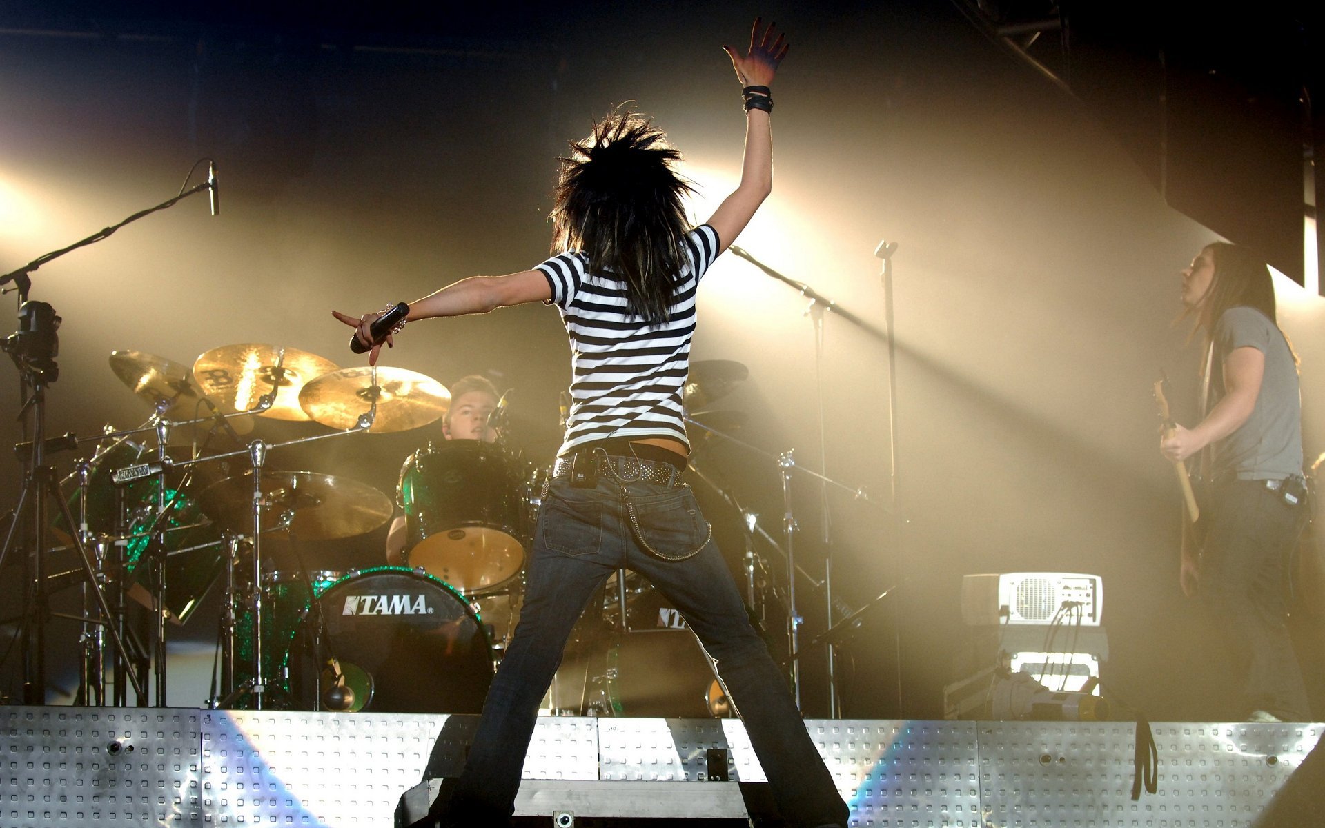 HD desktop wallpaper showing Tokio Hotel performing live on stage with dramatic lighting and a dynamic rock music atmosphere.
