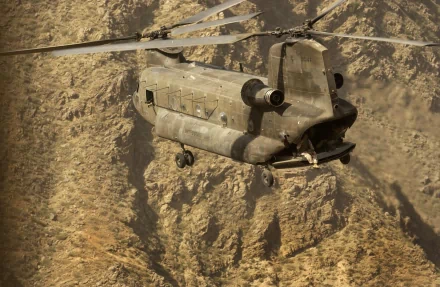 A HD wallpaper featuring a military Boeing CH-47 Chinook helicopter flying over a rugged mountainous terrain.