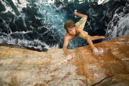 A climber ascends a rugged rock face above turbulent ocean waters, capturing the thrill of rock climbing in a dynamic HD desktop wallpaper.