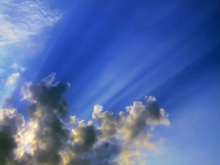 HD PC desktop wallpaper showcasing a vibrant blue sky with sun rays streaming through scattered clouds in a natural setting.