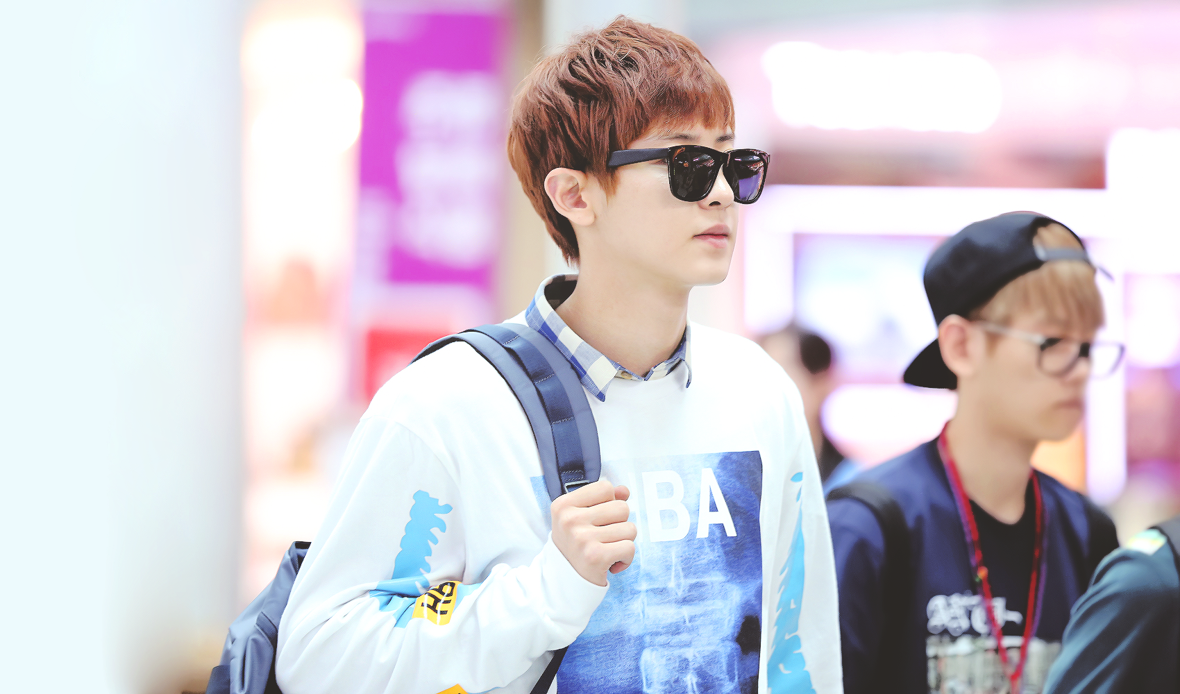 A stylish individual with sunglasses walks through an airport, showcasing a casual outfit. This HD desktop wallpaper captures the essence of music and EXO culture.