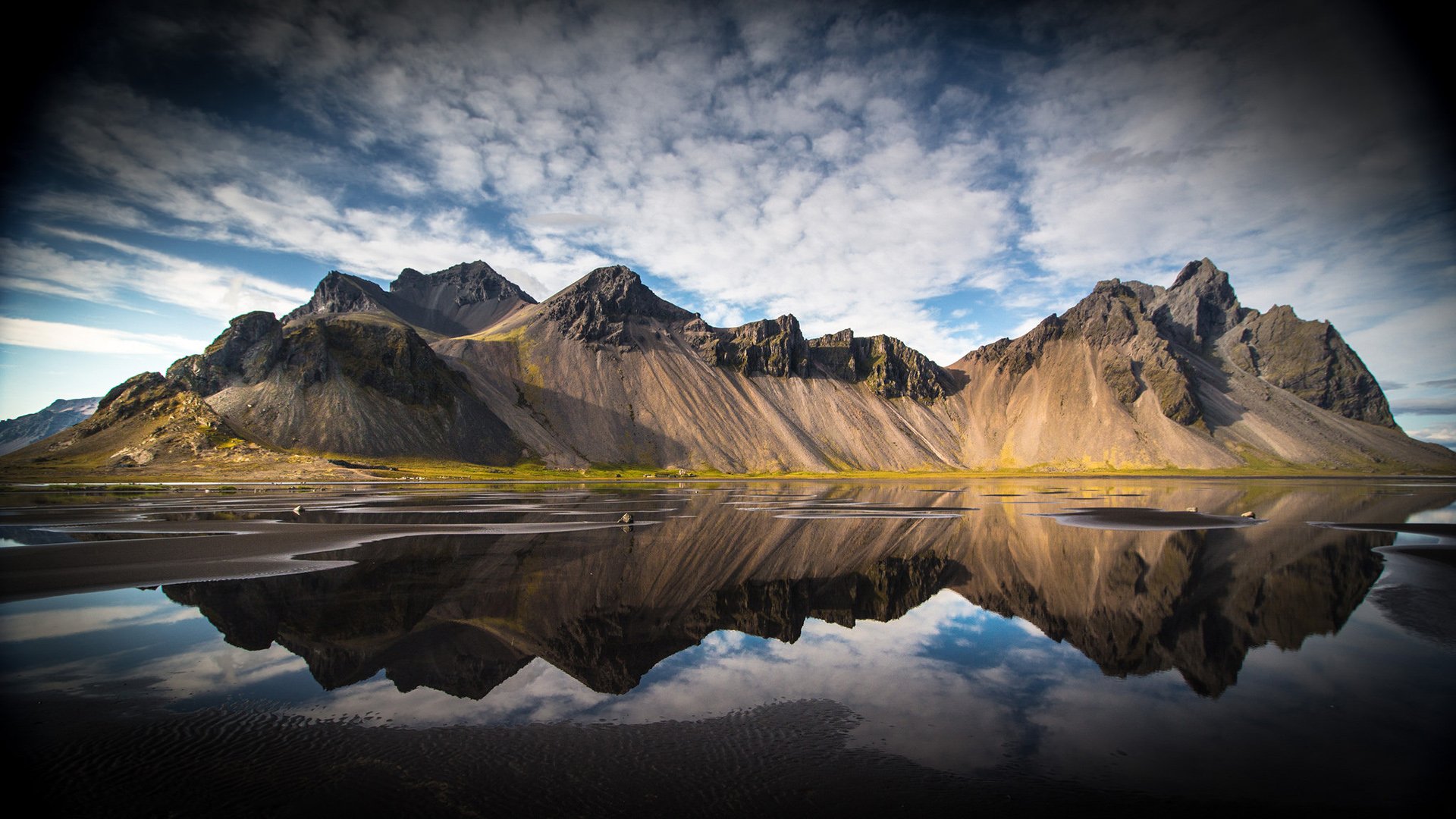 A stunning natural landscape featuring majestic mountains reflected in a calm body of water, set against a dramatic sky. This HD image serves as a captivating wallpaper and background.