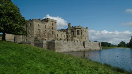 HD desktop wallpaper featuring the man-made Raby Castle beside a reflective moat under a blue sky with scattered clouds.