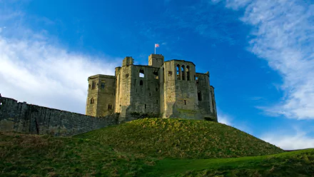 HD desktop wallpaper featuring Warkworth Castle, a historic man-made fortress set against a vibrant blue sky.