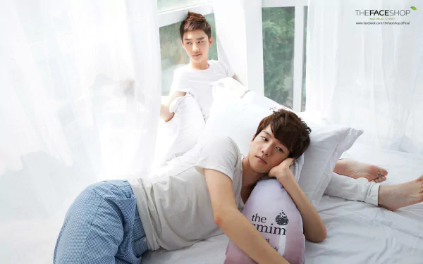 A serene HD desktop wallpaper featuring two members of EXO relaxing in soft, white surroundings, conveying a tranquil and cozy atmosphere.