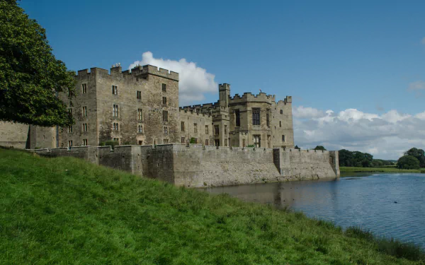 HD desktop wallpaper featuring the man-made Raby Castle beside a reflective moat under a blue sky with scattered clouds.