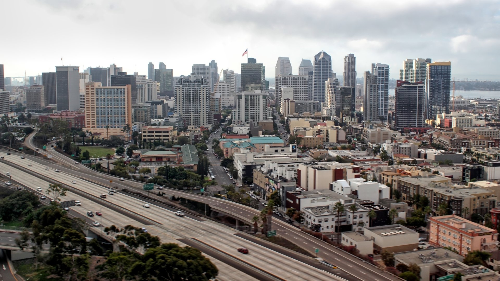 HD desktop wallpaper showcasing a man-made urban skyline of San Diego with highways and dense city buildings under a cloudy sky.