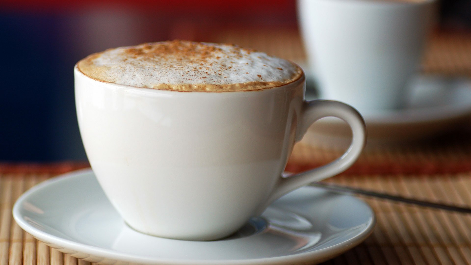 A close-up of a cappuccino in a white cup on a saucer, showcasing its creamy froth and dusting of cocoa. This HD image serves as a rich, inviting desktop wallpaper.