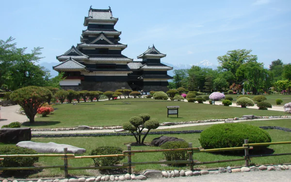 HD PC desktop wallpaper: Matsumoto Castle, a man-made black-walled fortress framed by manicured Japanese gardens under a clear blue sky.