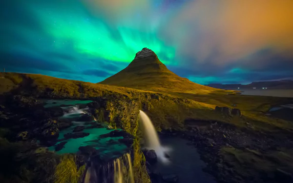 HD wallpaper of the aurora borealis illuminating the sky above a majestic mountain and cascading waterfall.