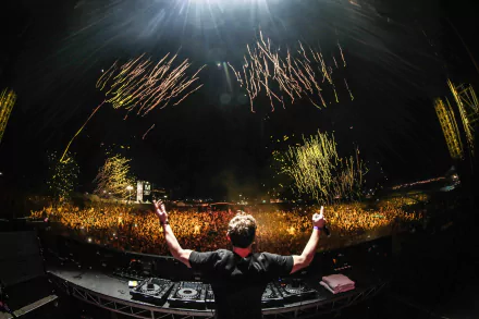 An electrifying HD desktop wallpaper featuring DJ Hardwell on stage, surrounded by a cheering crowd and vibrant fireworks, capturing the excitement of live music events.