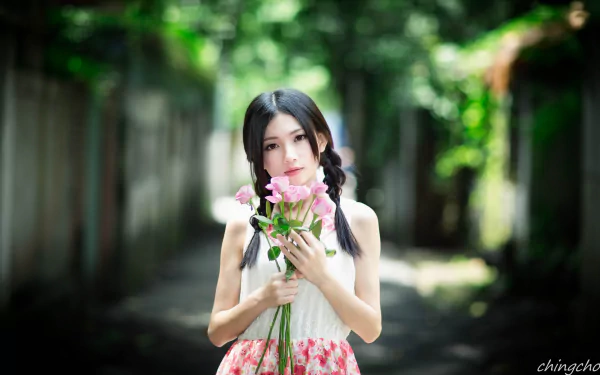 HD desktop wallpaper featuring an Asian model with black hair holding pink flowers. The background showcases a soft focus, highlighting the detailed depth of field in a shaded outdoor alley.