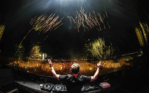 An electrifying HD desktop wallpaper featuring DJ Hardwell on stage, surrounded by a cheering crowd and vibrant fireworks, capturing the excitement of live music events.