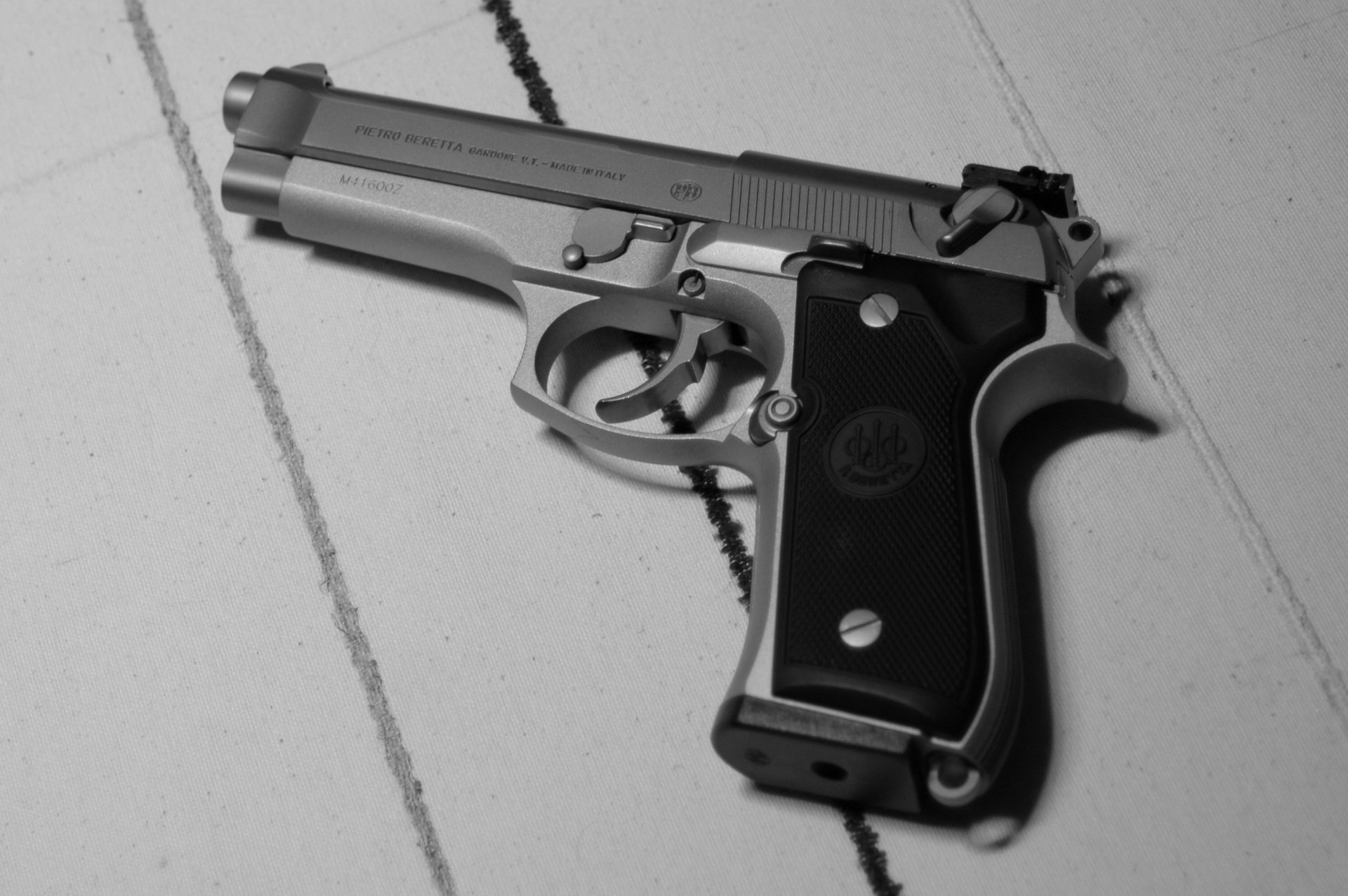 Black and white HD desktop wallpaper of a Beretta handgun resting on a tiled surface, highlighting the man-made firearm's detailed craftsmanship.
