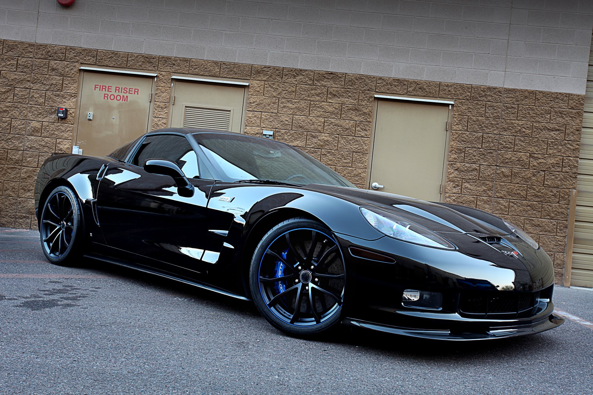 Black Chevrolet Corvette ZR1 vehicle parked against a brick wall, glossy finish and blue-accent rims — 4K Ultra HD PC desktop wallpaper/background.