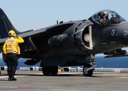 A sailor salutes next to a McDonnell Douglas AV-8B Harrier II on the flight deck of the USS Bataan (LHD-5), showcasing military aviation on a clear day.