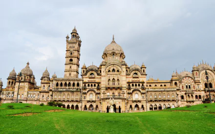 HD wallpaper showcasing the grand man-made Laxmi Vilas Palace in Vadodara against a cloudy sky and lush green lawn foreground.
