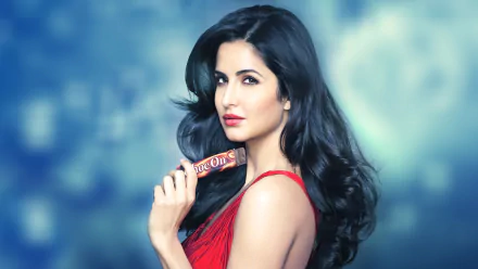 HD desktop wallpaper featuring Bollywood actress Katrina Kaif, dressed in red, with long brunette hair, holding a product against a blurred blue background.