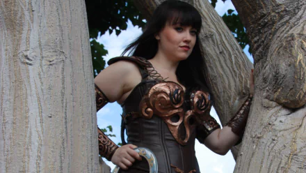 Cosplay of Xena from Xena: Warrior Princess, featuring a woman in a detailed warrior outfit, posing elegantly among trees, showcasing strength and confidence in HD quality.