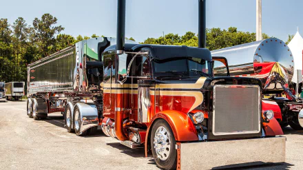 HD desktop wallpaper featuring a shiny orange and black Peterbilt truck parked beside a trailer under clear skies.