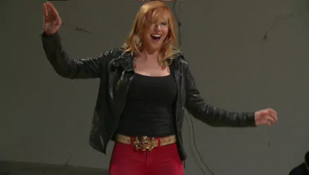 HD desktop wallpaper of a smiling red‑haired celebrity in a black leather jacket and red pants, arms outstretched against a plain, neutral background.