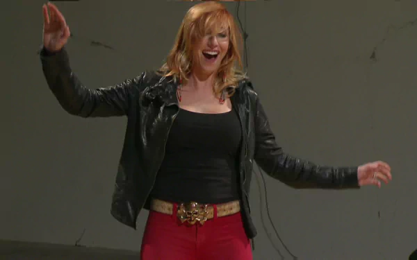 HD desktop wallpaper of a smiling red‑haired celebrity in a black leather jacket and red pants, arms outstretched against a plain, neutral background.
