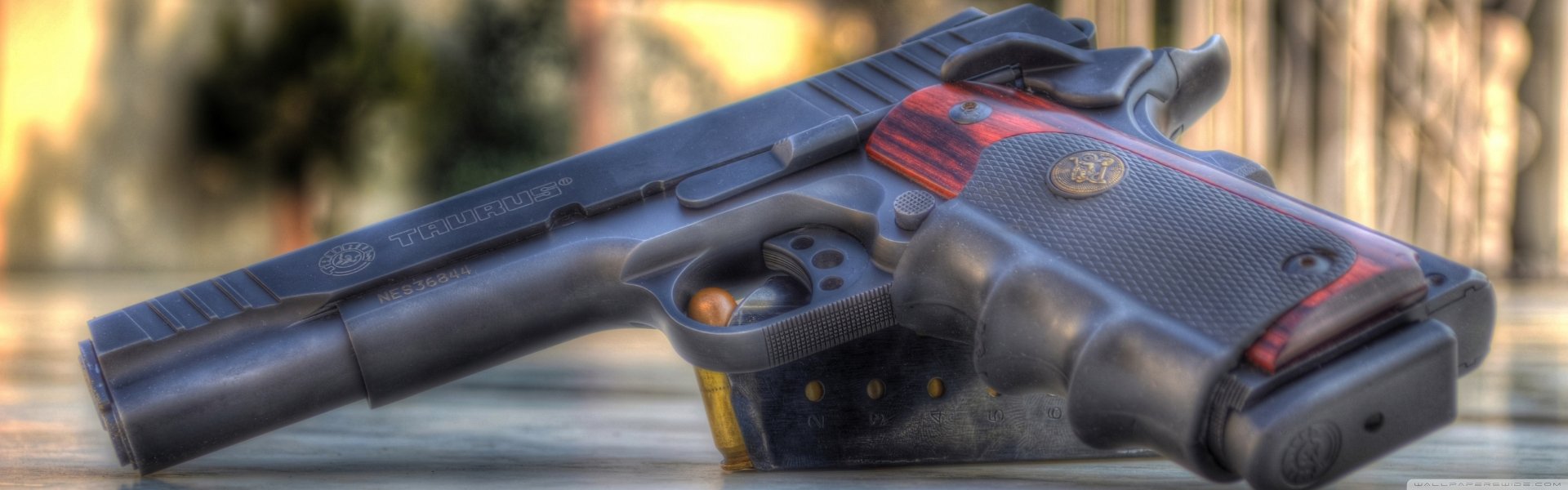 HD PC desktop wallpaper: close-up of a man-made Taurus pistol with wood-accented grip and visible brass cartridges against a soft, blurred background.