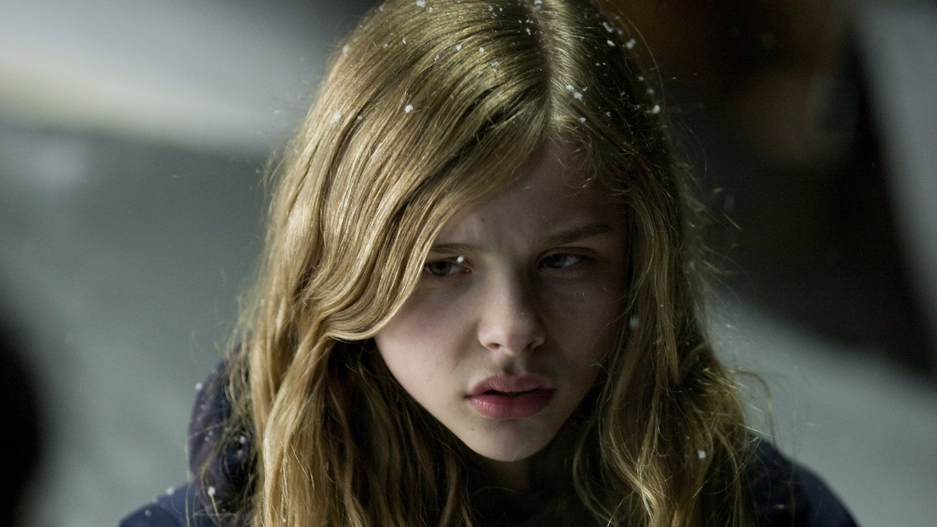 HD desktop wallpaper from the movie Let Me In, featuring a close-up of a young girl with long blonde hair and a serious expression in a dimly lit setting.